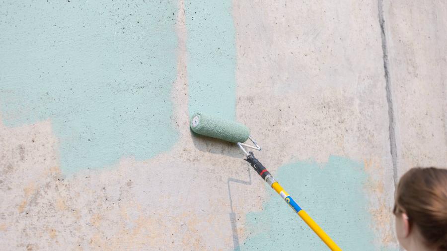 A blank cement wall is primed with paint with a roller brush.