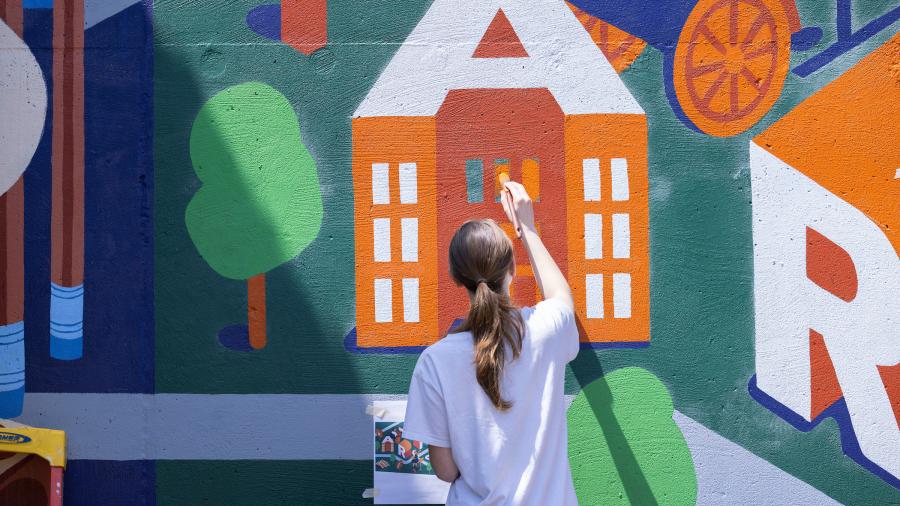 A student paints a large letter 'A' on a mural. 
